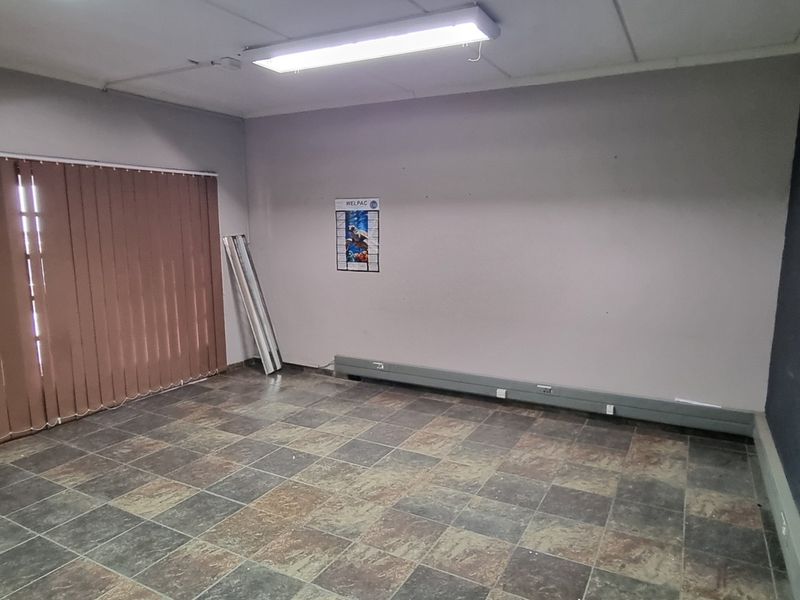An empty industrial office space featuring tiled flooring, fluorescent lighting, and vertical blinds, suitable for a variety of commercial or administrative uses.