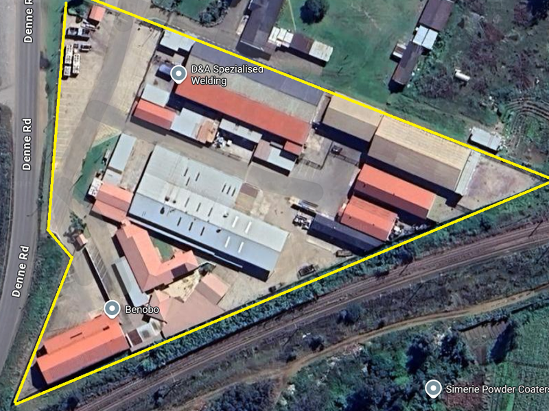 Aerial view of an industrial property complex featuring multiple warehouse structures, metal roofing, and paved yard space with access to adjacent road and rail infrastructure.