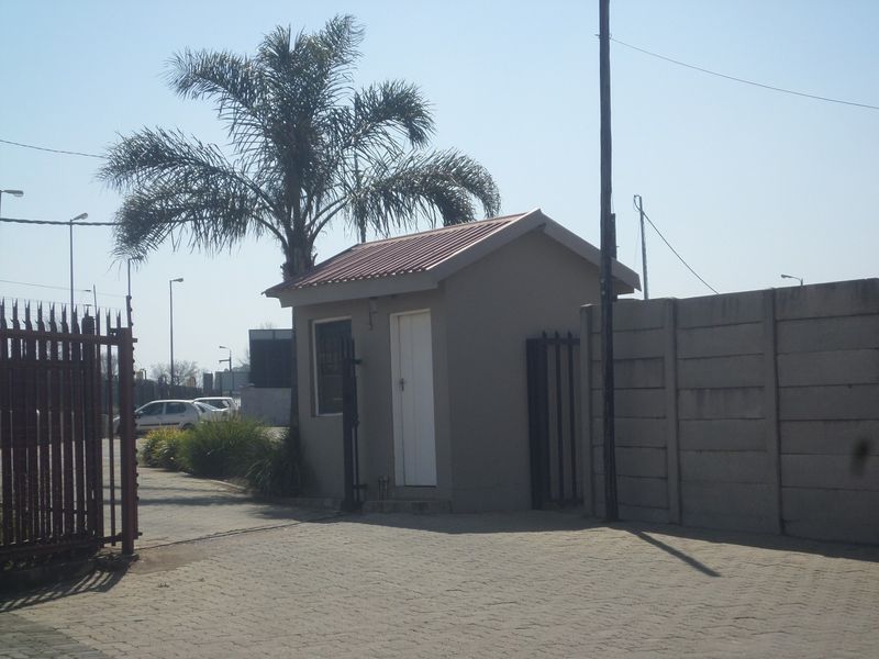A functional security guard house located at the property entrance, featuring a pitched metal roof, paved driveway, and secure perimeter fencing.