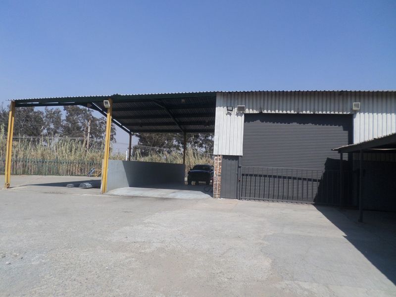 Industrial property exterior featuring a large covered loading bay, roller shutter door access, and expansive concrete hardstand area.