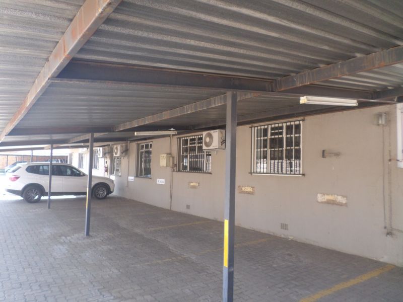 Covered parking area featuring a corrugated metal roof, steel support structure, paved flooring, and wall-mounted air conditioning units for the adjacent industrial units.