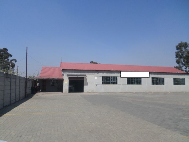Front elevation of an industrial warehouse featuring a corrugated metal roof, paved yard area, and secure boundary walling.