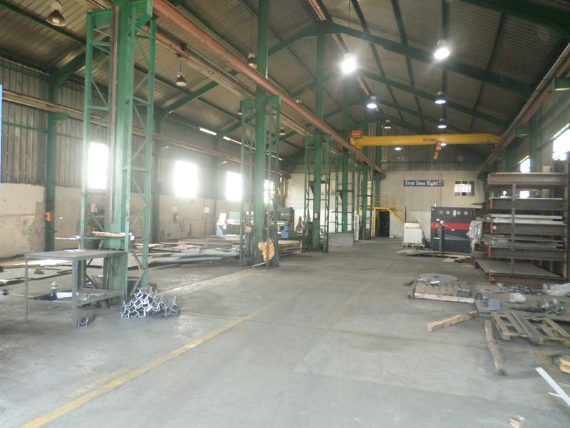 Spacious industrial warehouse featuring high ceilings, overhead crane system, robust steel structural columns, and durable concrete flooring suitable for manufacturing or storage operations.
