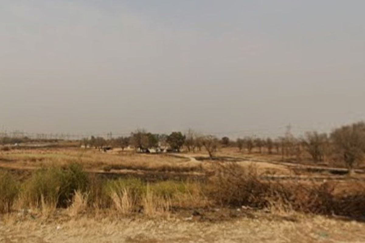 A wide landscape view of the farm property featuring open fields and natural vegetation under a hazy sky.