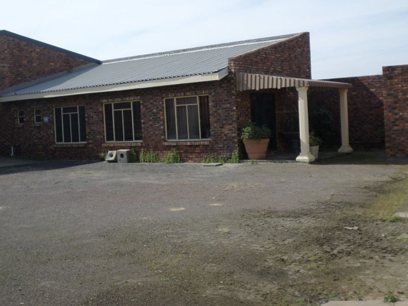 Front exterior view of an industrial property featuring a face brick facade, corrugated metal roof, roller shutter door, and a covered entrance porch.
