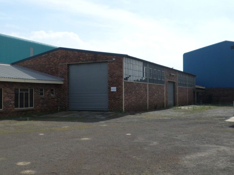 Industrial property featuring brick exterior walls, multiple roller shutter doors, and a large asphalt yard area suitable for logistics or manufacturing operations.