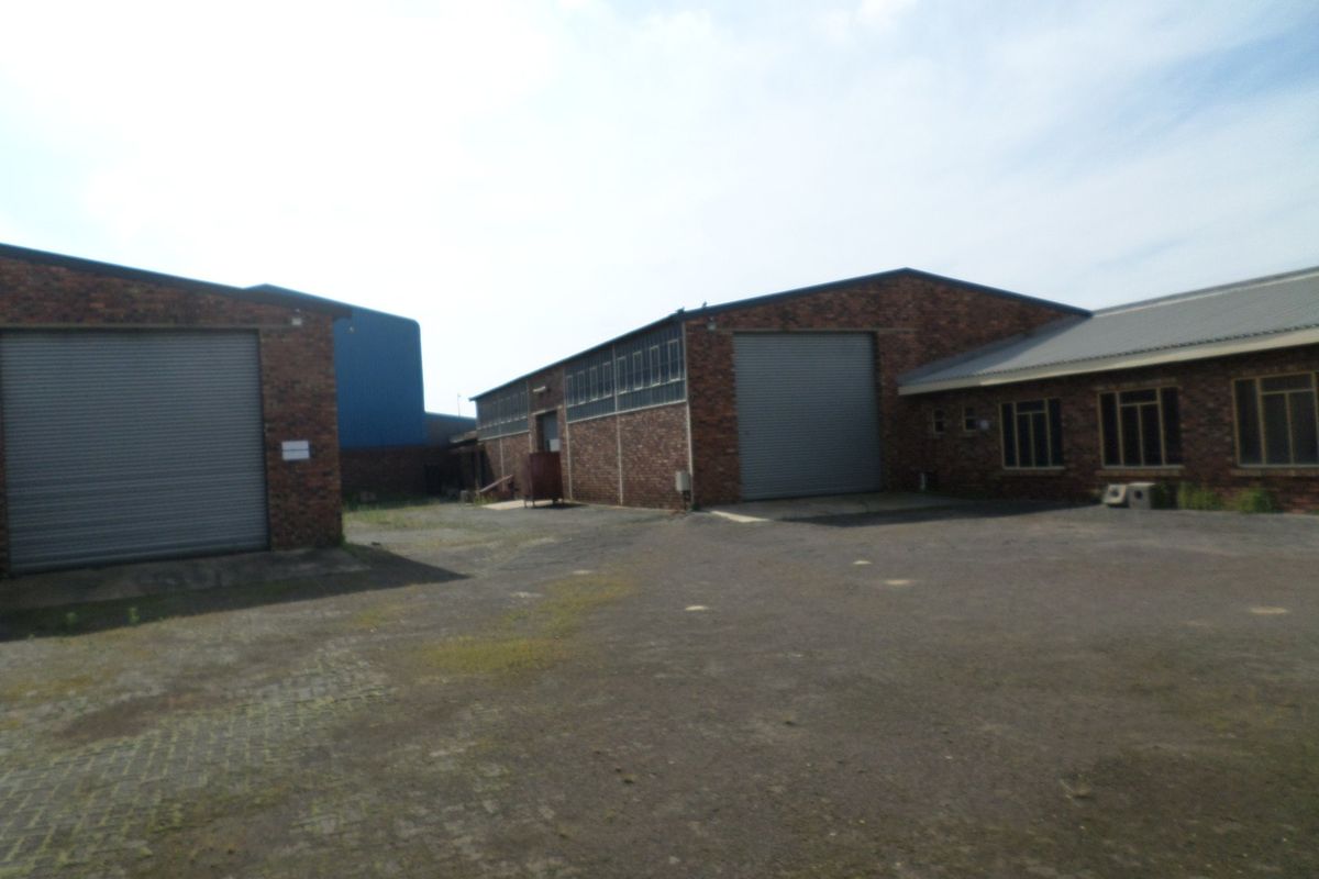 Exterior view of an industrial property featuring multiple roller shutter doors, brick facade, and a large paved yard area.