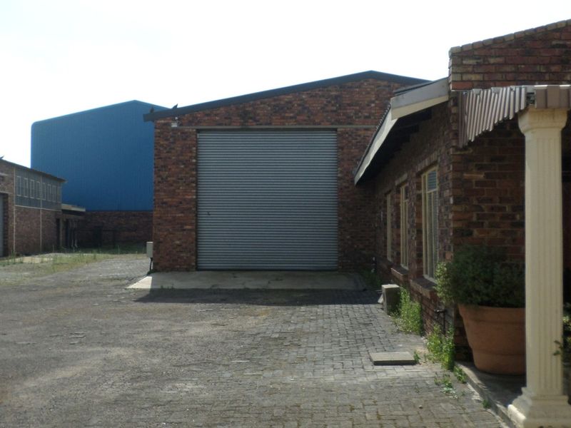 Exterior view of an industrial property featuring a large roller shutter door, brick facade, and paved yard area.