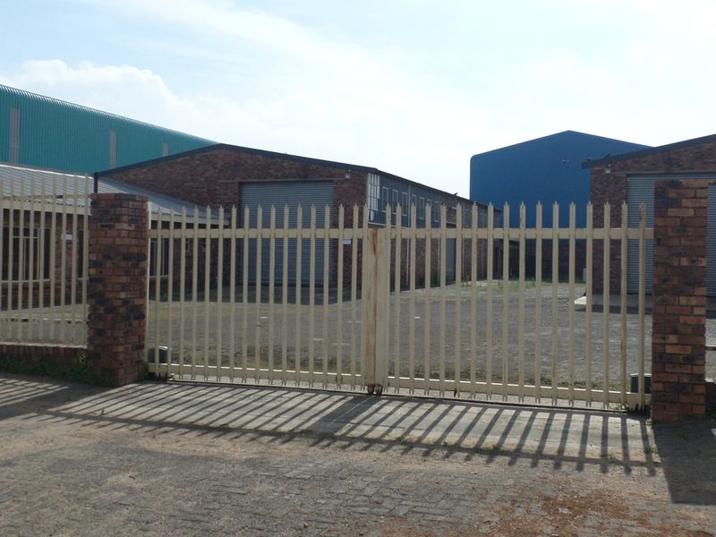 Industrial property frontage featuring secure steel palisade fencing, brick pillars, and multiple metal roller shutter doors for warehouse access.