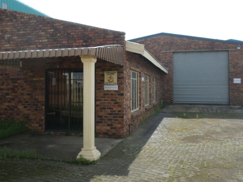 Industrial property featuring a face brick facade, a large roller shutter door for vehicle access, and a covered entrance area with paved driveway.