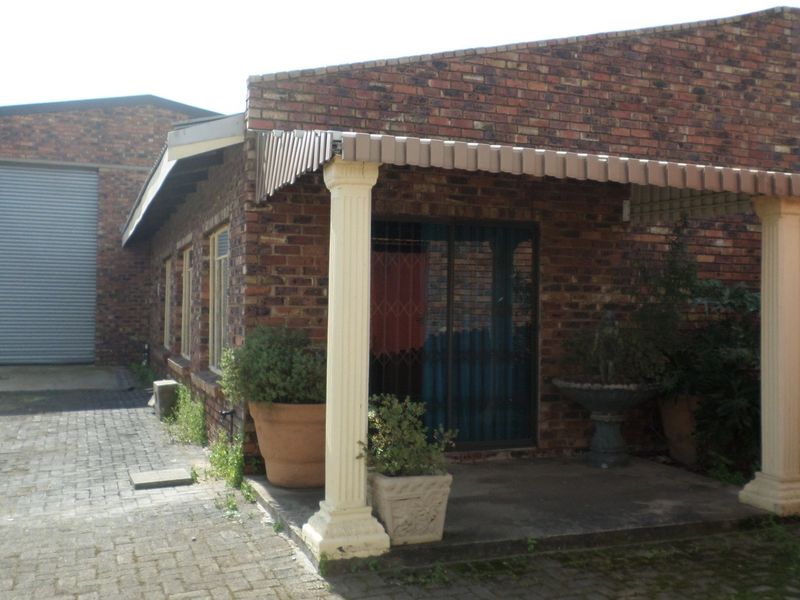 Industrial property exterior featuring a brick facade, a large roller shutter door, and a covered patio area with decorative columns.