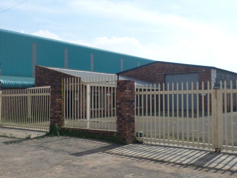 Front view of an industrial property featuring a face brick facade, roller shutter door, and secure steel palisade fencing with a brick perimeter wall.