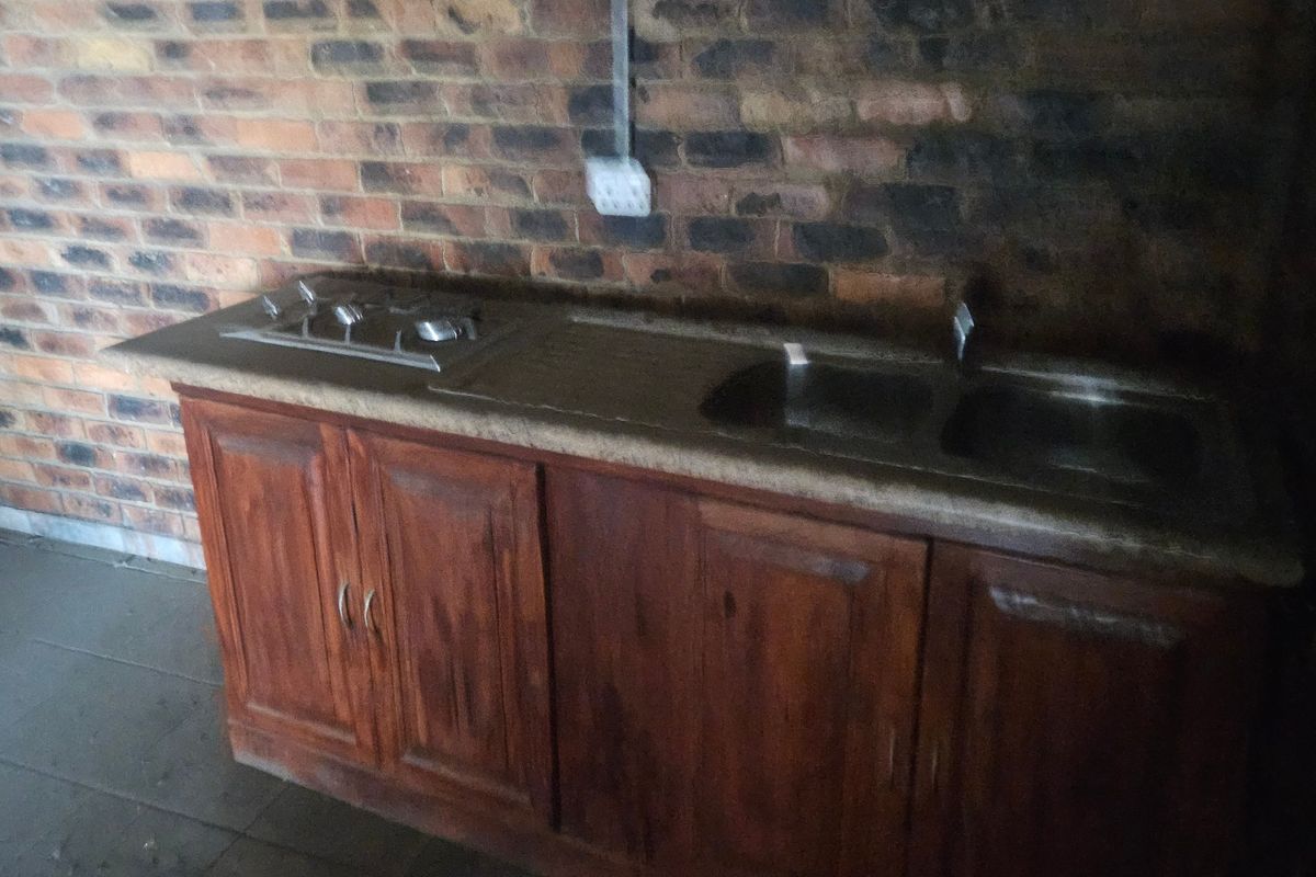 A basic kitchenette featuring exposed brick walls, wooden cabinetry, a stainless steel double sink, and a built-in gas hob.