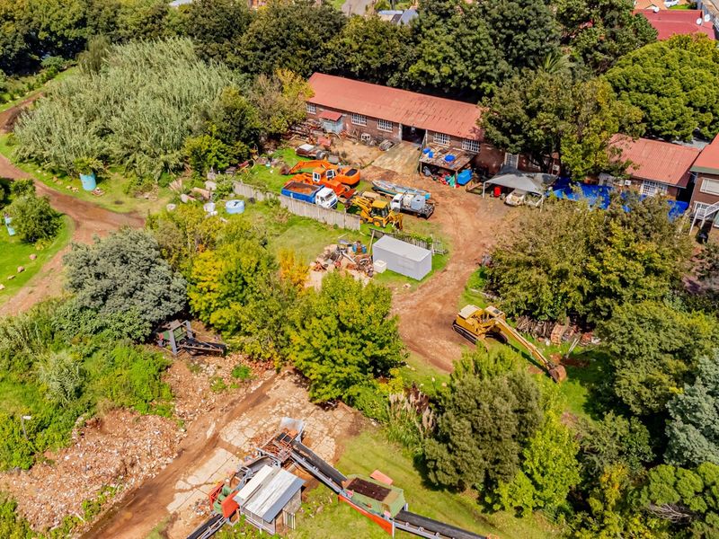 Aerial view of a commercial property featuring a warehouse structure, extensive outdoor storage space, and unpaved access areas surrounded by mature trees.