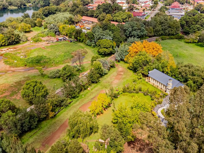 Aerial view of a large commercial vacant land plot featuring mature trees, landscaped grounds, and an existing building structure.