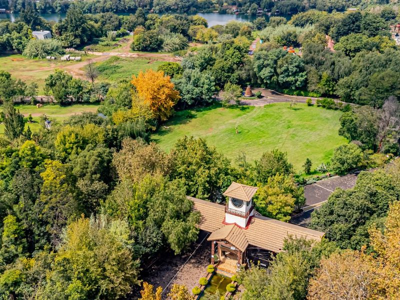 Aerial view of a commercial property featuring a clock tower entrance, paved driveway, water feature, and extensive landscaped grounds with mature trees.