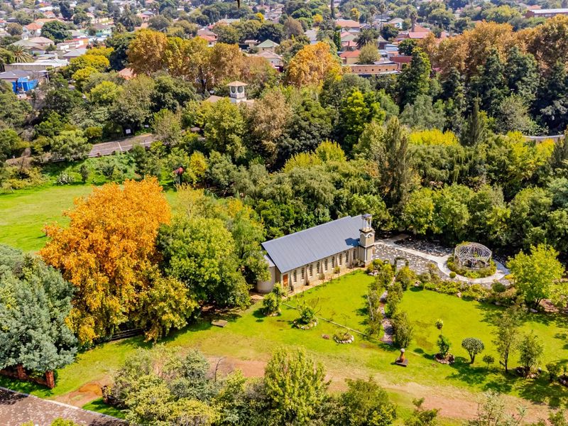 Aerial view of a commercial property featuring a stone building set within a lush, mature garden with paved pathways and a gazebo.
