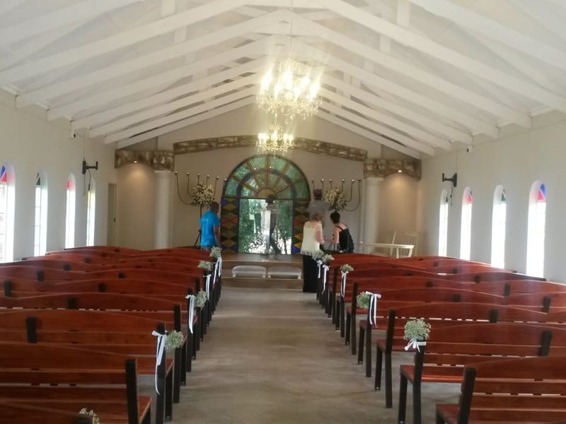 A spacious event hall featuring a high vaulted ceiling with exposed rafters, arched windows, and a decorative stone-framed stained glass feature at the altar.