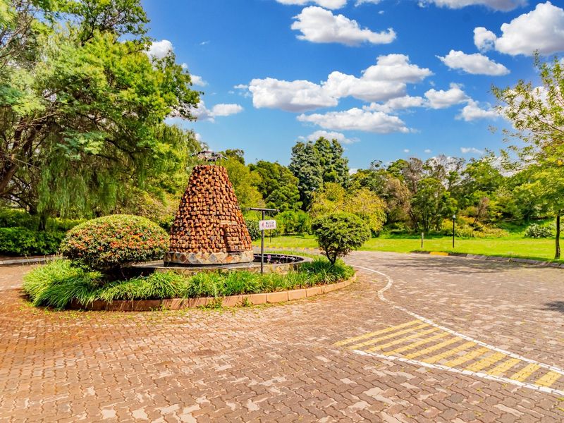 A well-maintained commercial property entrance featuring a paved driveway, landscaped gardens, and a central brick fountain feature.