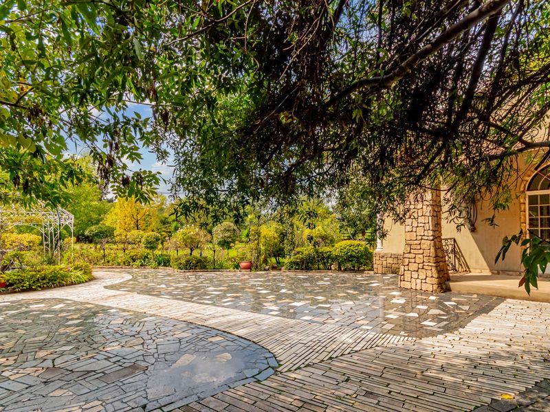 A beautifully landscaped rear garden featuring a stone-paved patio, brick pathways, a decorative wrought iron gazebo, and an arched entrance to the building.