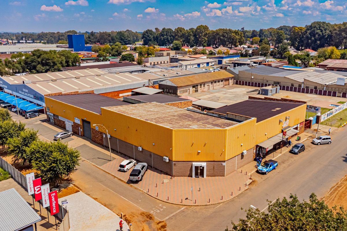 Aerial view of a corner industrial property featuring extensive warehouse space, paved parking, and multiple access points in a commercial business district.