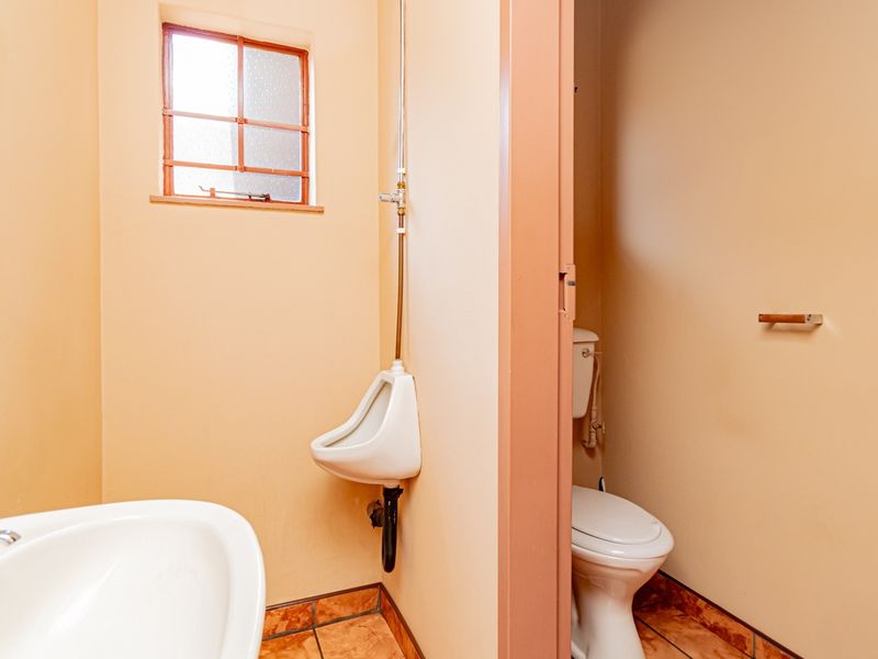 A functional industrial bathroom featuring a wall-mounted urinal, a standard toilet, and a washbasin with tiled flooring.