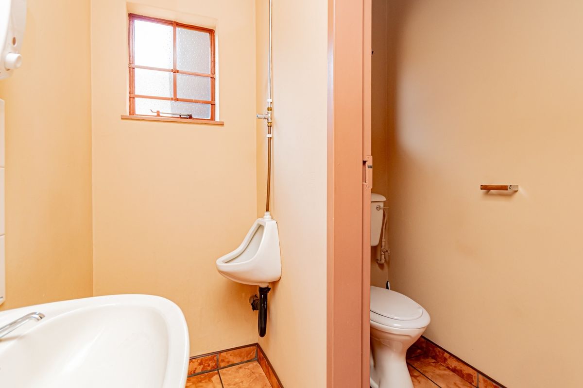 A functional industrial bathroom featuring a wall-mounted urinal, a standard toilet, and a washbasin with tiled flooring.