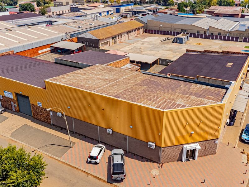Aerial view of an industrial property featuring corrugated metal roofing, brick facade, roller shutter doors, and a paved parking area.