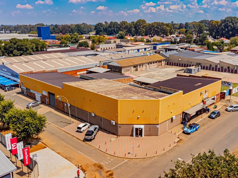 Aerial view of a corner industrial property featuring extensive warehouse space, paved parking, and multiple access points in a commercial business district.
