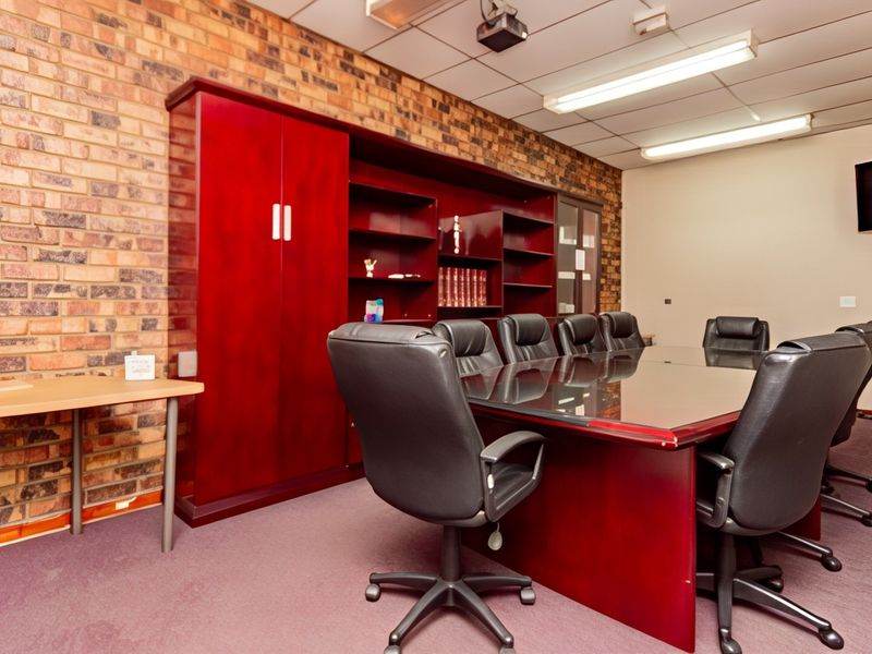 A professional office or boardroom featuring an exposed brick feature wall, built-in storage cabinetry, and a suspended ceiling with integrated lighting.