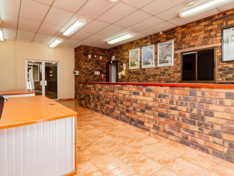 A professional office reception area featuring exposed brick walls, tiled flooring, a built-in reception counter, and suspended ceiling lighting.