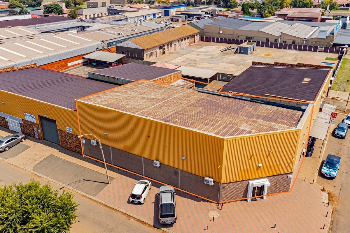 Aerial view of an industrial property featuring corrugated metal roofing, brick facade, roller shutter doors, and a paved parking area.