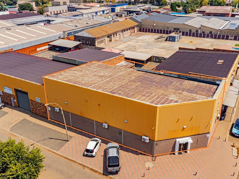 Aerial view of an industrial property featuring corrugated metal roofing, brick facade, roller shutter doors, and a paved parking area.