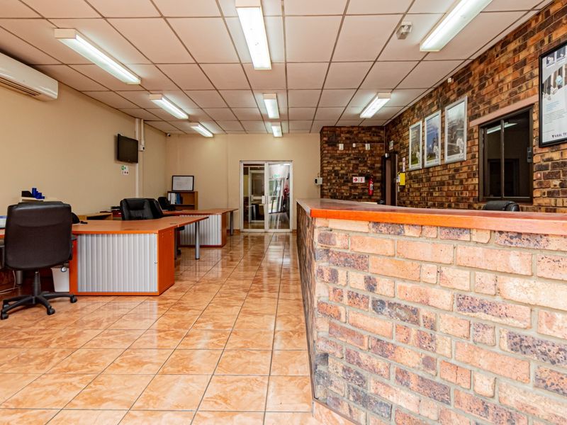 Spacious industrial office area featuring a brick reception counter, ceramic tile flooring, suspended ceiling, and integrated air conditioning.