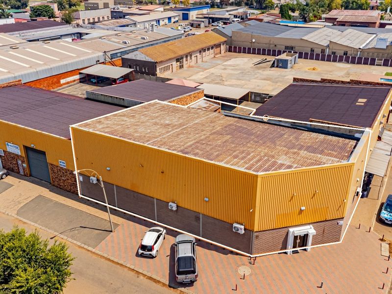 Aerial view of an industrial property featuring corrugated metal roofing, brick facade, roller shutter doors, and a paved parking area.