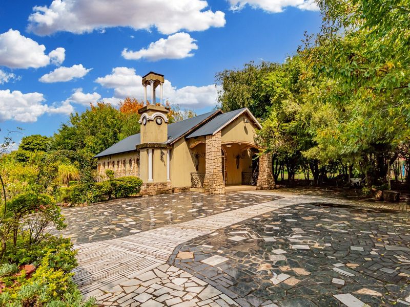A charming commercial building featuring a bell tower, stone-clad pillars, and a well-maintained paved driveway surrounded by lush garden landscaping.
