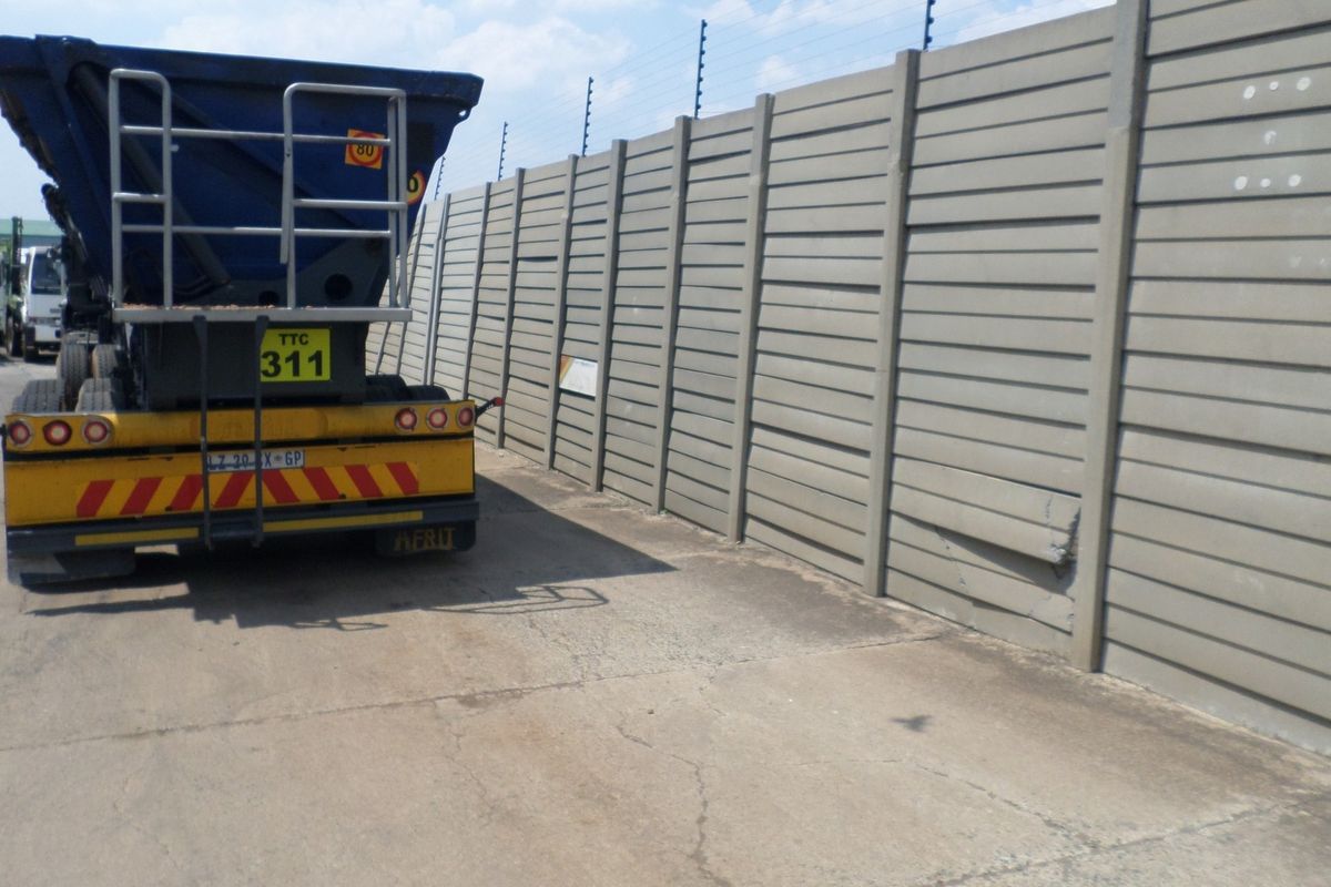 Industrial yard area featuring a precast concrete boundary wall with electric fencing and a concrete hardstand surface showing signs of wear.