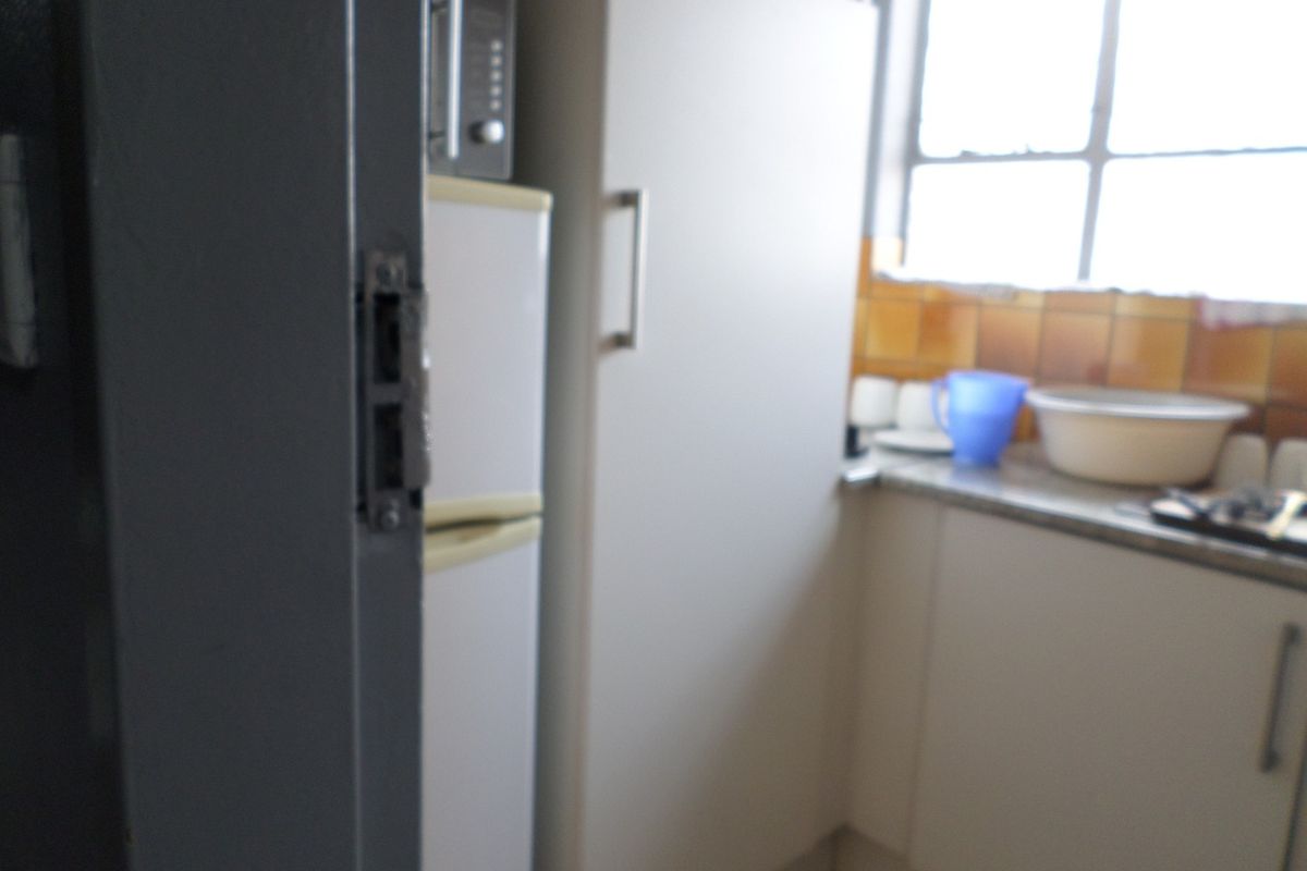 A small kitchen area featuring built-in cabinetry, a tiled backsplash, and a countertop, currently showing signs of age and wear.