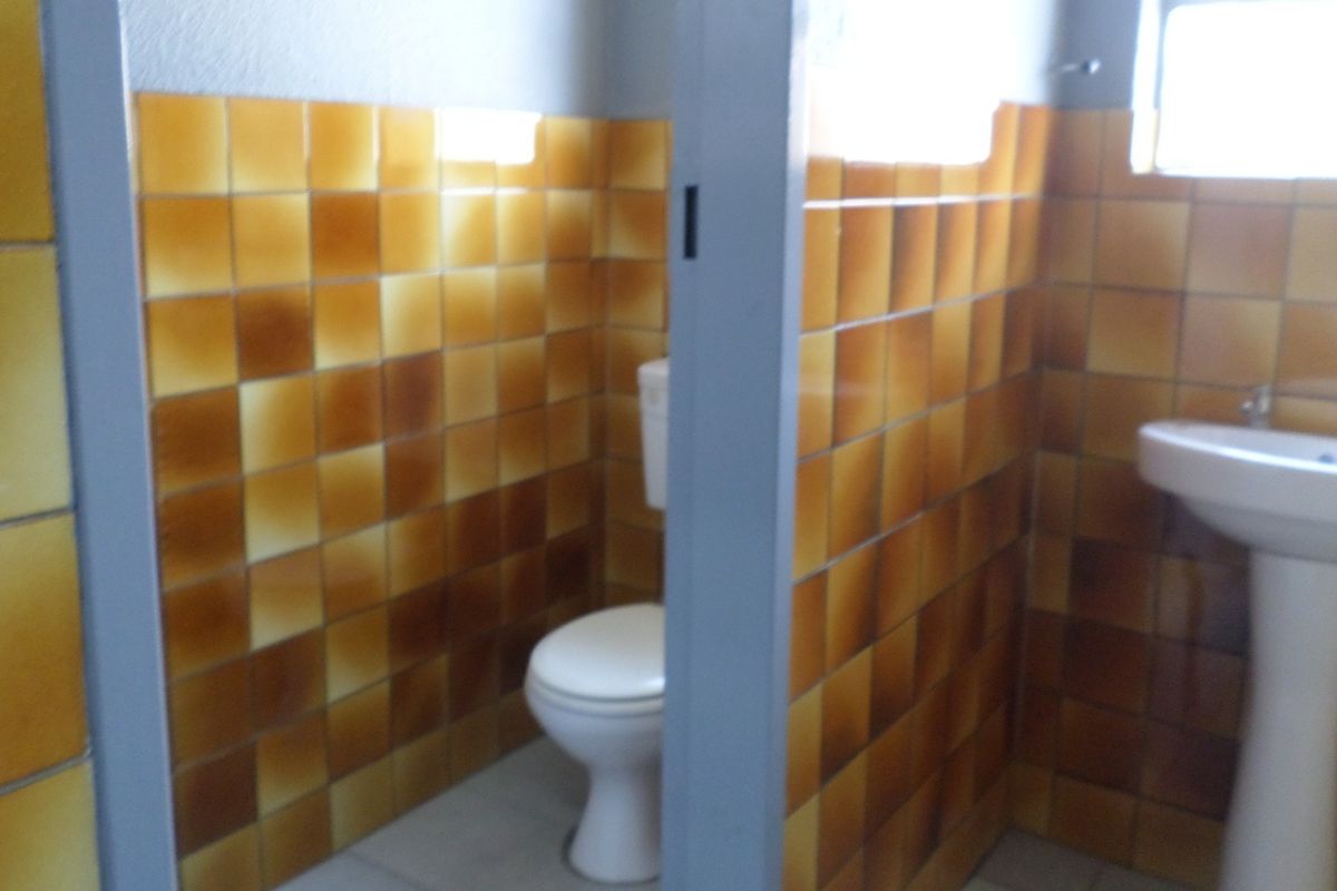 A functional bathroom featuring a pedestal basin and toilet with dated ceramic wall tiling.