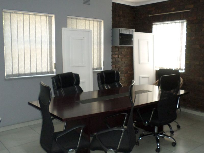 A functional office space featuring exposed brick walls, tiled flooring, and vertical blinds, suitable for a professional meeting or workspace environment.