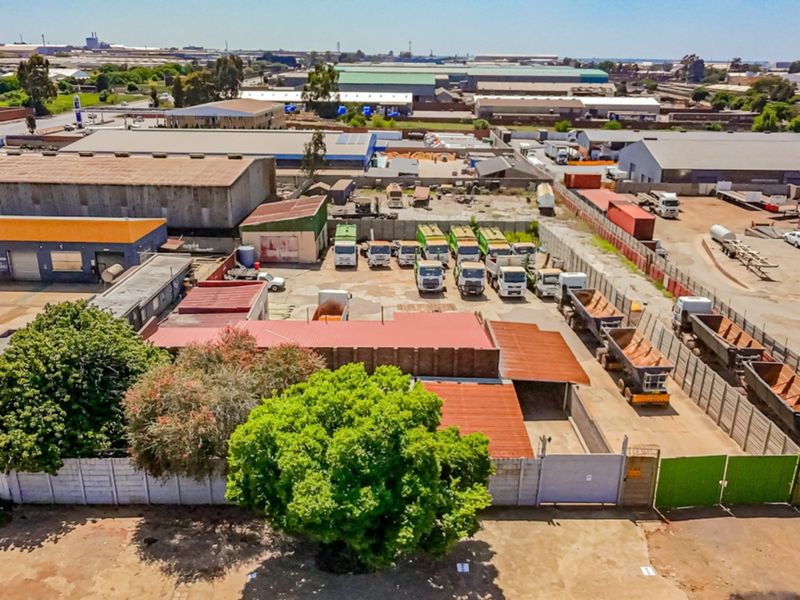 Aerial view of an industrial property featuring multiple warehouse buildings, a paved yard area, and perimeter security fencing in an established industrial zone.