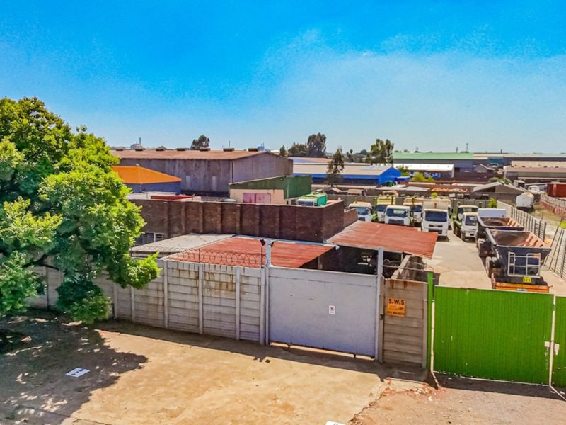 Aerial view of an industrial property featuring a secure yard, precast concrete boundary walls, and metal access gates with corrugated roofing structures.
