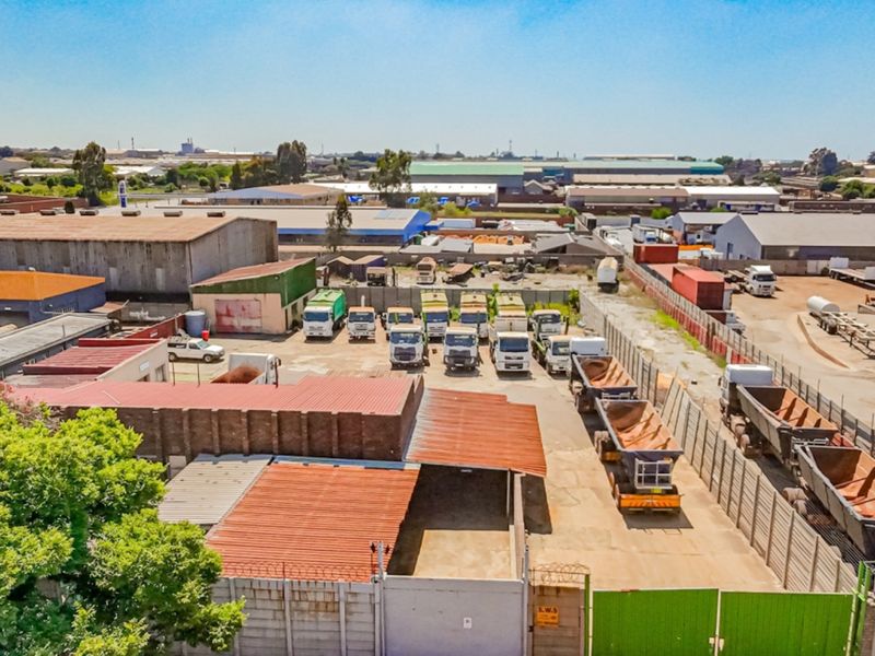 Aerial view of an industrial property featuring a paved yard, secure perimeter walling, and multiple warehouse structures with metal roofing.