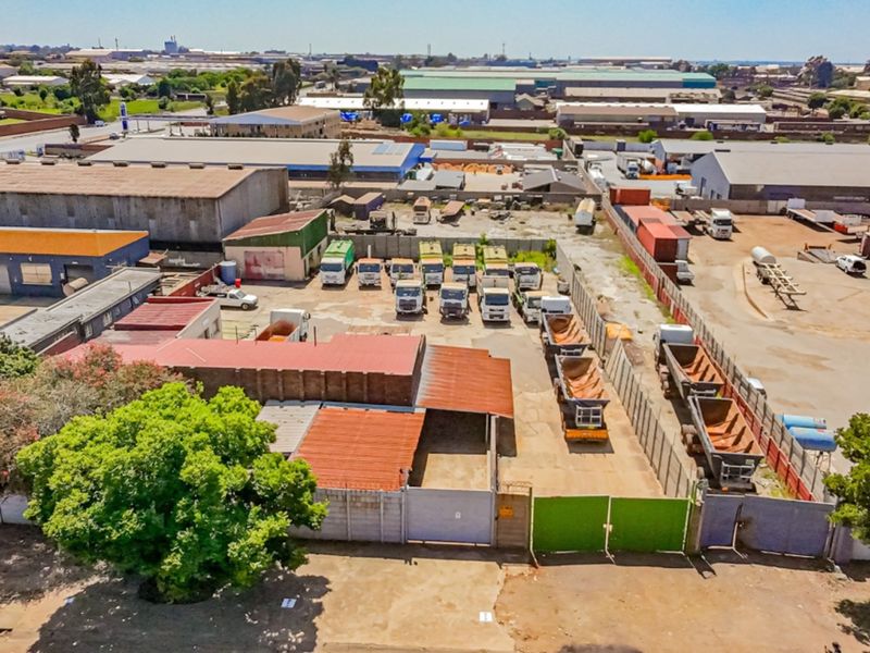 Aerial view of an industrial property featuring multiple warehouse buildings, a secure fenced yard, and extensive paved parking areas for heavy vehicles.