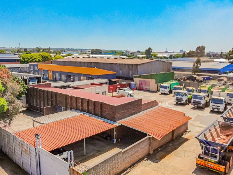 Aerial view of an industrial property featuring warehouse structures, paved yard space, and covered parking bays within a secure perimeter.