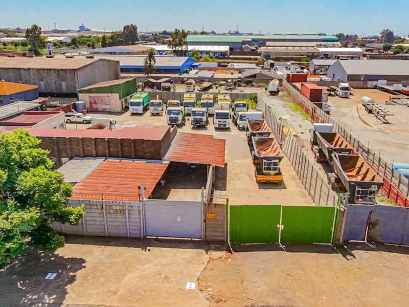 Aerial view of an industrial property featuring a secure yard, perimeter fencing, and multiple warehouse structures with corrugated metal roofing.