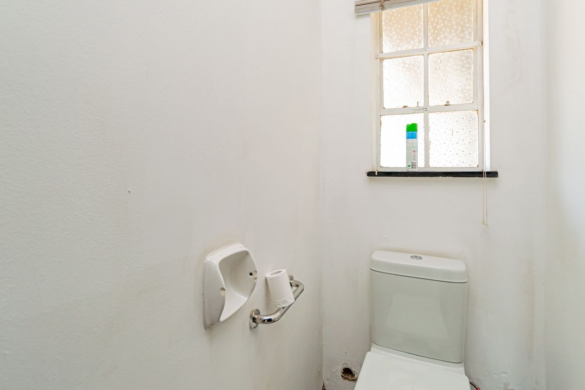 A small, functional bathroom featuring a standard toilet, wall-mounted soap dish, and a window with natural light.