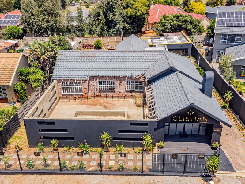 Aerial view of a property featuring a tiled roof, chimney, and an unfinished exterior brick facade section, set within a residential neighbourhood.
