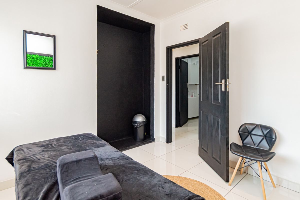 A bedroom featuring tiled flooring, a built-in black alcove, and access to an adjoining room through a dark-toned door.