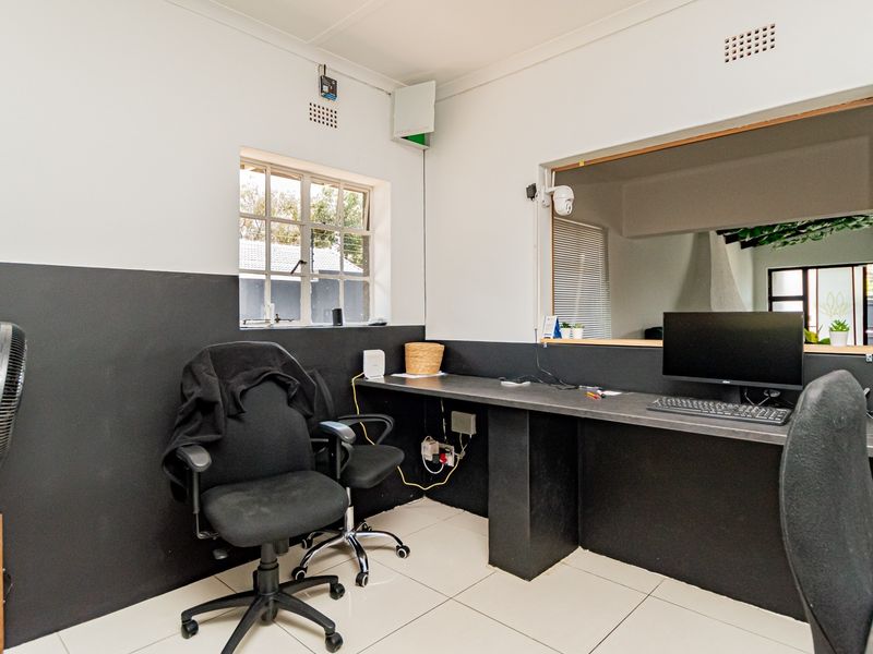 A functional home office space featuring a built-in desk, tiled flooring, and an internal window providing natural light and visibility into adjacent areas.